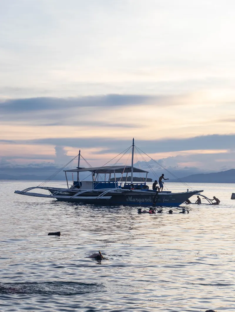 An outrigger banca boat and snorkelers in calm water off Moalboal