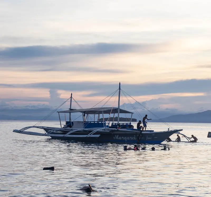 An outrigger banca boat and snorkelers in calm water off Moalboal