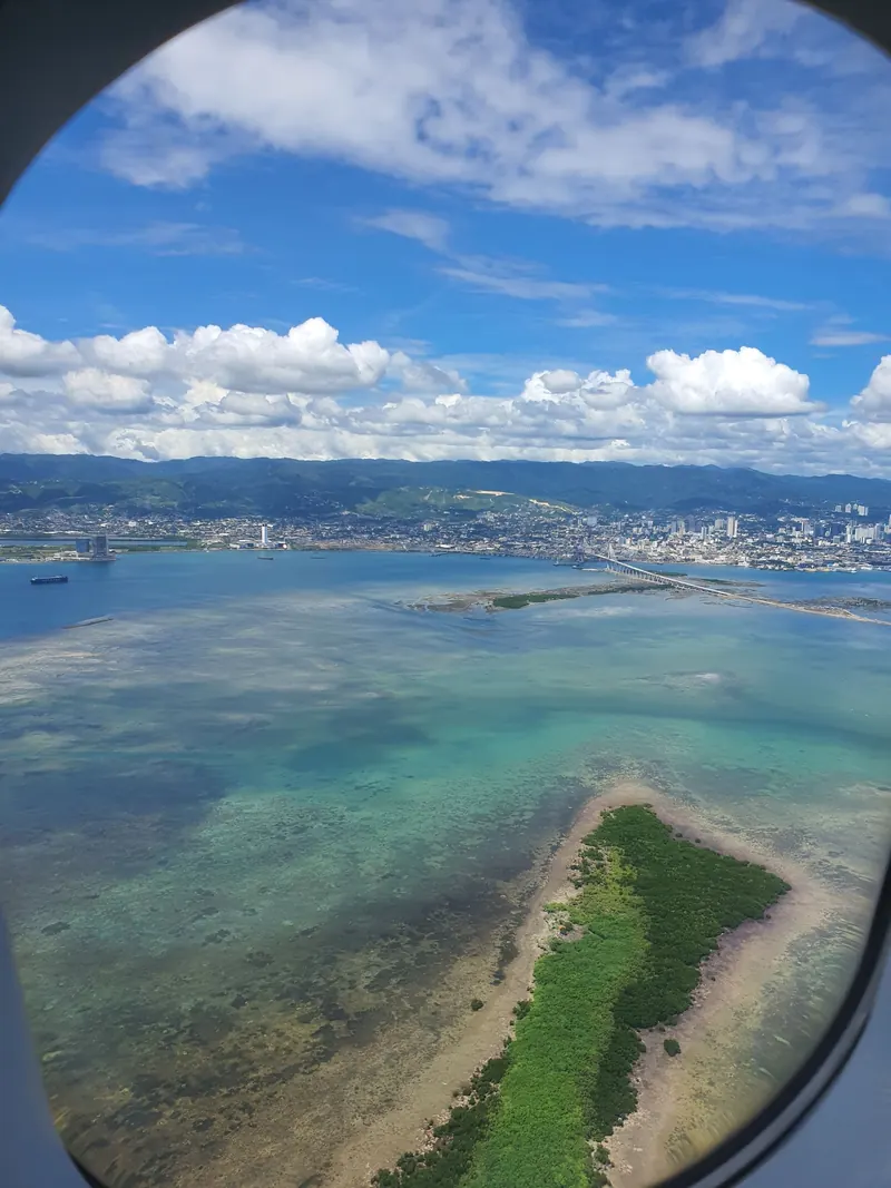 Aerial view of the Cebu coastline and turquoise shallows seen through an airplane window
