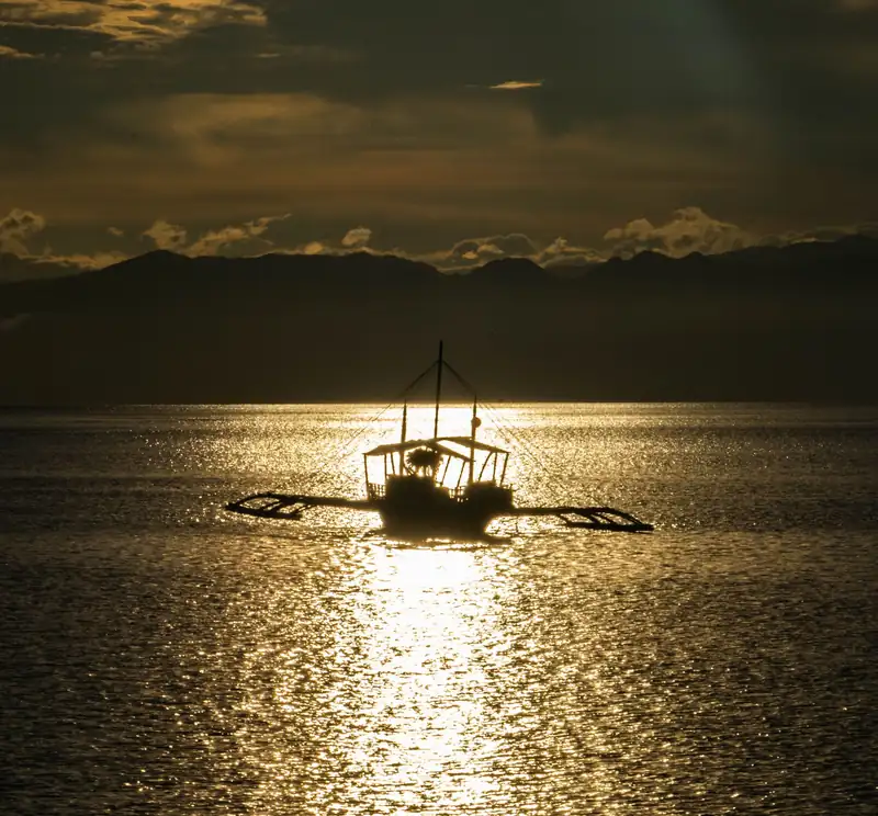 Silhouette of a banca boat on golden water at sunset in Moalboal