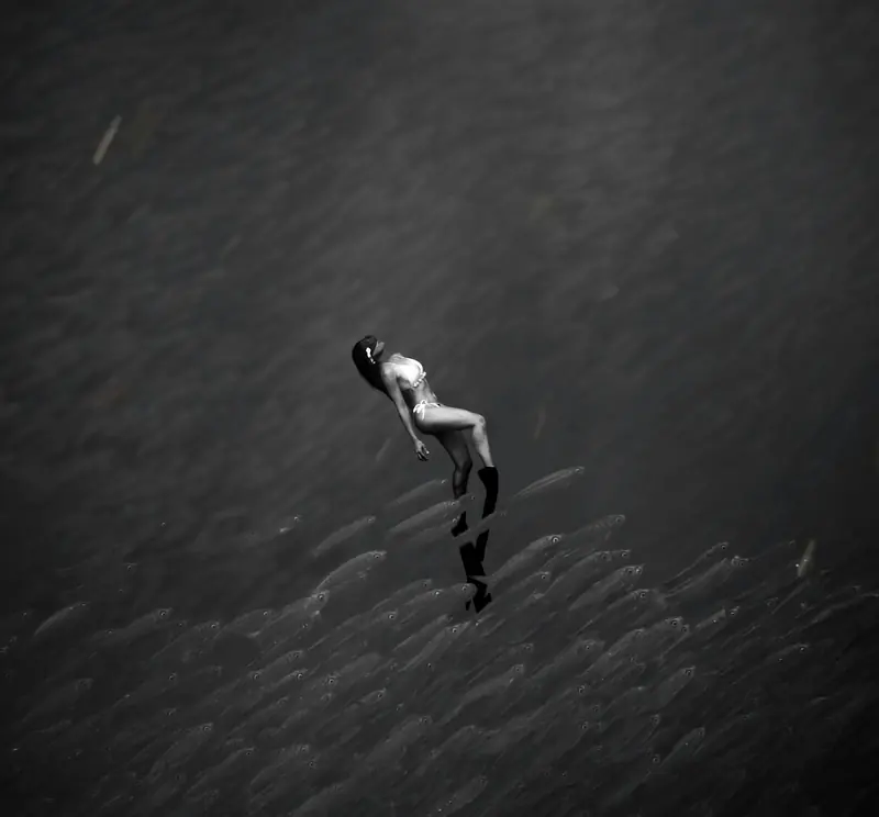 A freediver swimming above a huge school of sardines off Moalboal, black and white